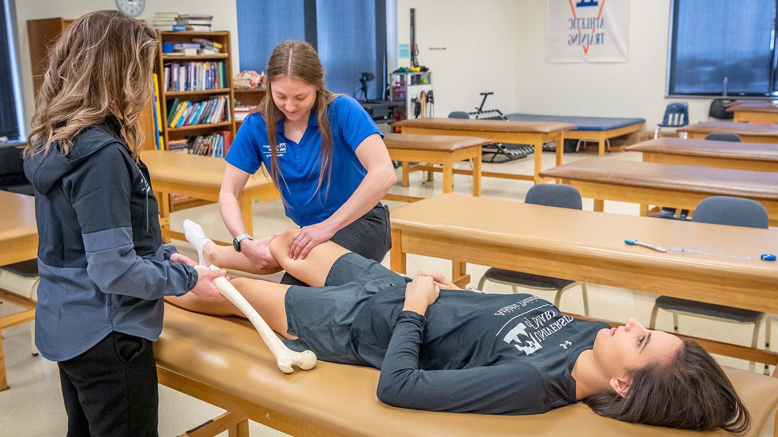 Athletic training student completing an 评估 on athlete’s knee while instructor is watching